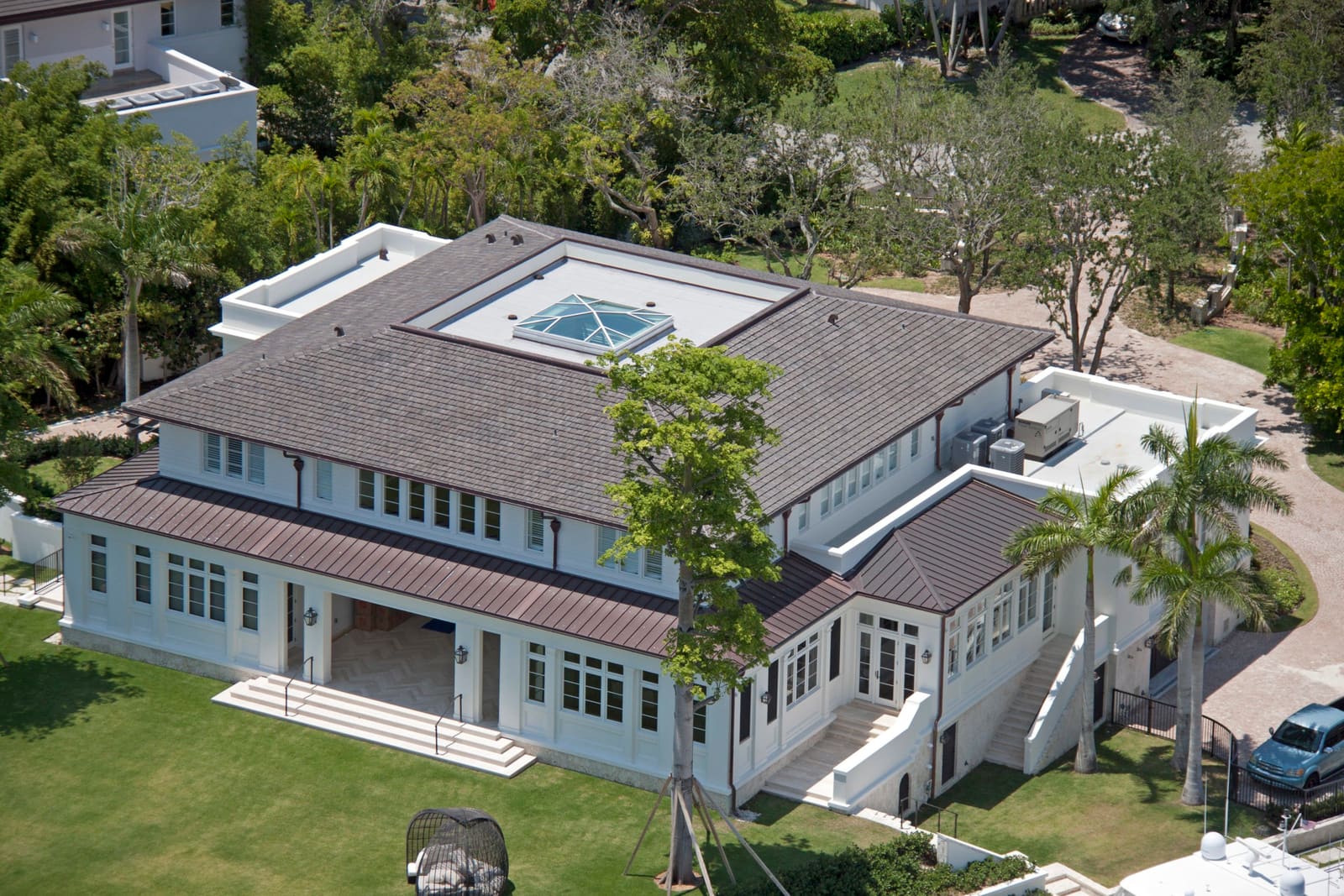 A finished traditional skylight set into the low-slope roof of a South Florida home, bordered by tile and standing-seam metal roofing, aerial view