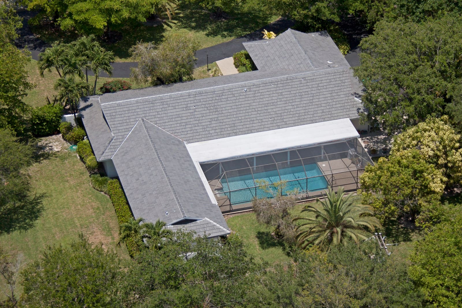 Pinecrest estate with a gray Crown concrete tile roof, screened pool, and mature canopy, aerial view.
