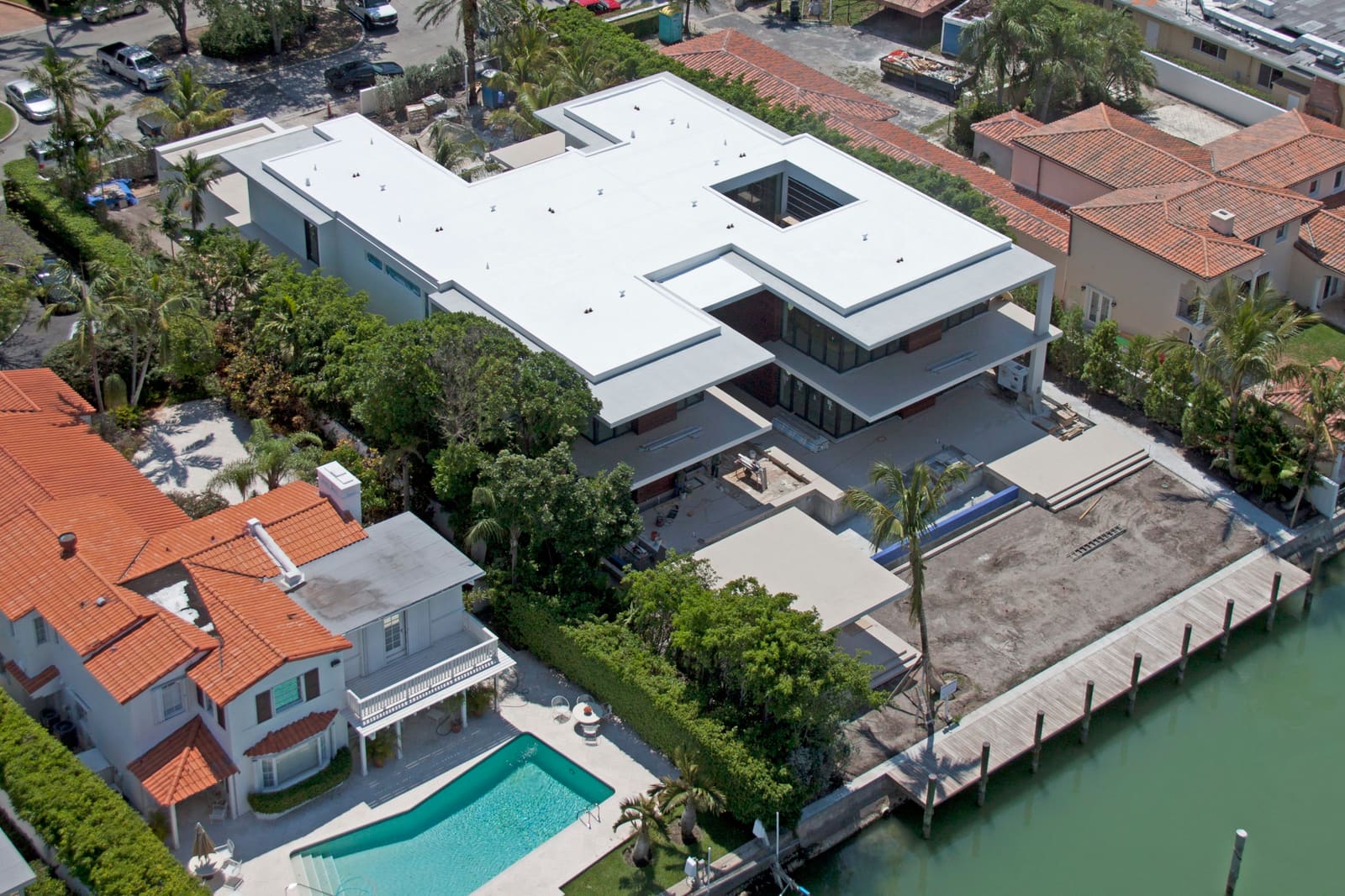 Aerial view of a large modernist home with a white TPO flat membrane roof beside the water.