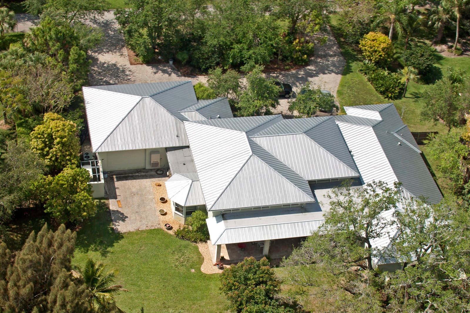 Completed galvalume standing-seam metal roof on a Pinecrest estate, hipped rooflines under the village tree canopy.