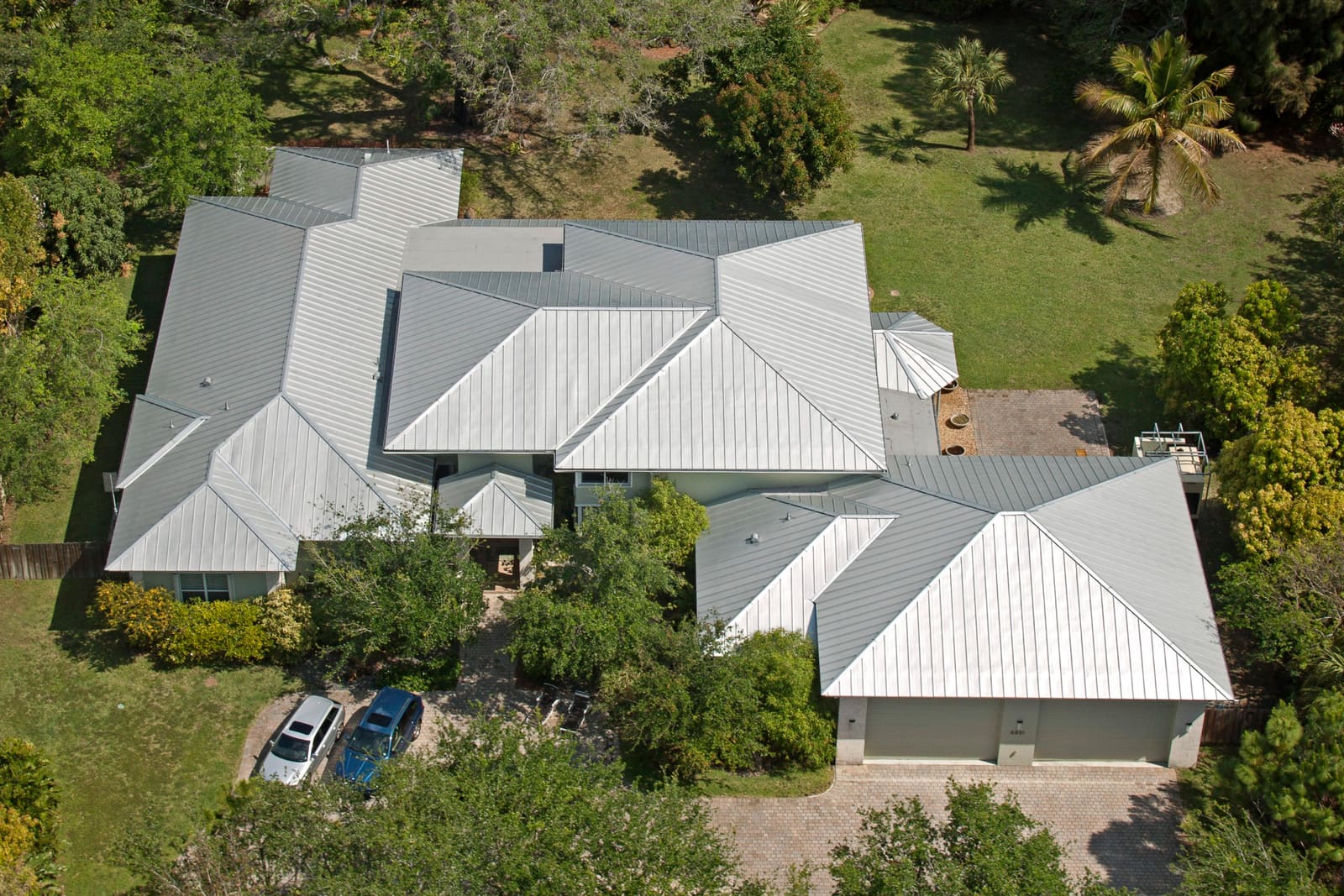 Aerial view of a silver standing-seam metal roof on a Pinecrest home set among mature shade trees