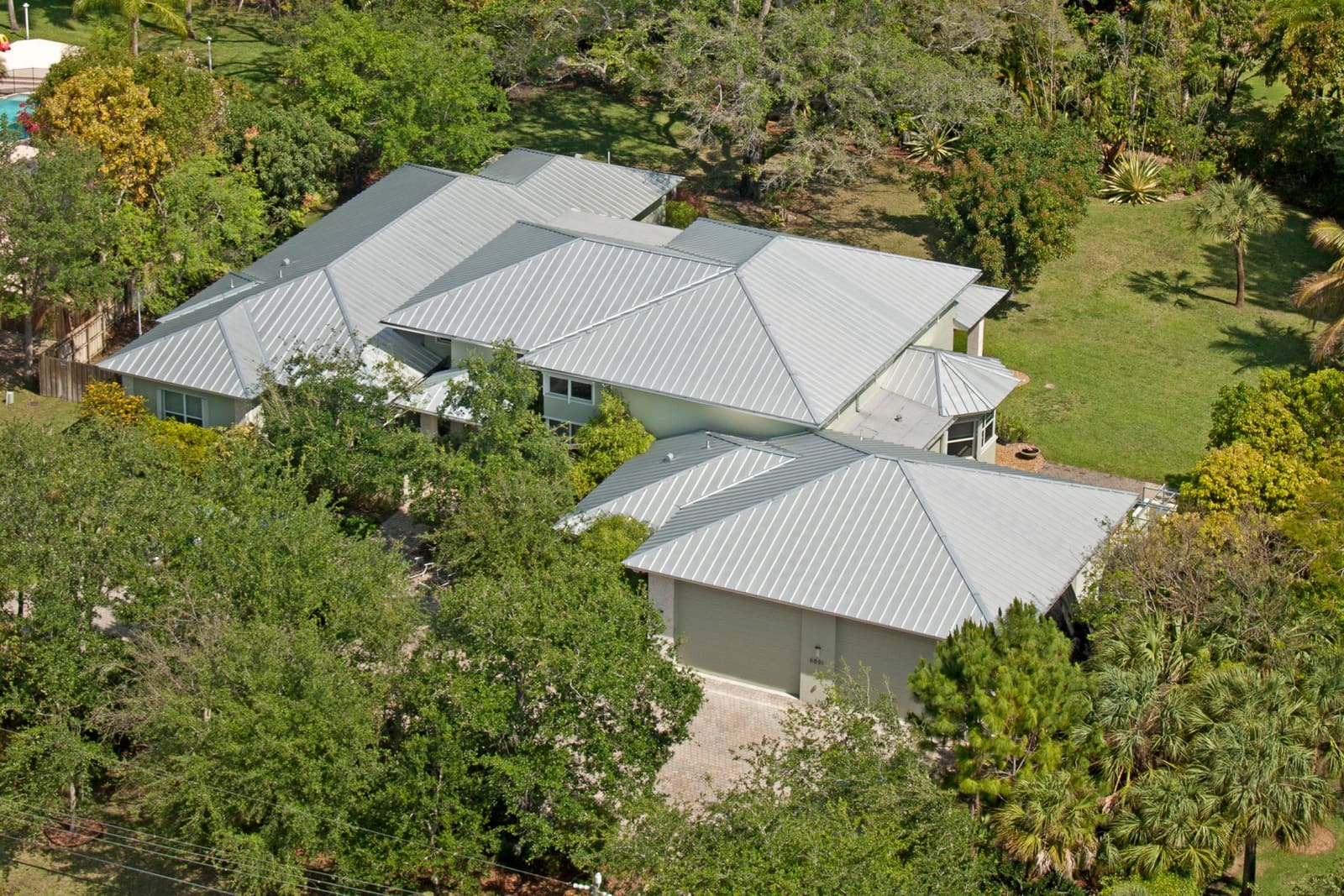 Galvalume standing-seam metal roof on a Pinecrest estate, aerial view of the completed installation among mature tropical landscaping.