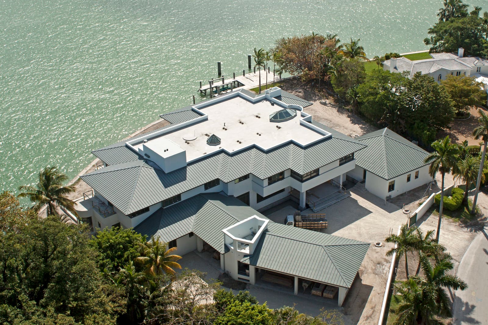 Aerial view of standing-seam metal hip roofs around a flat center deck on a bayfront estate in Miami Beach