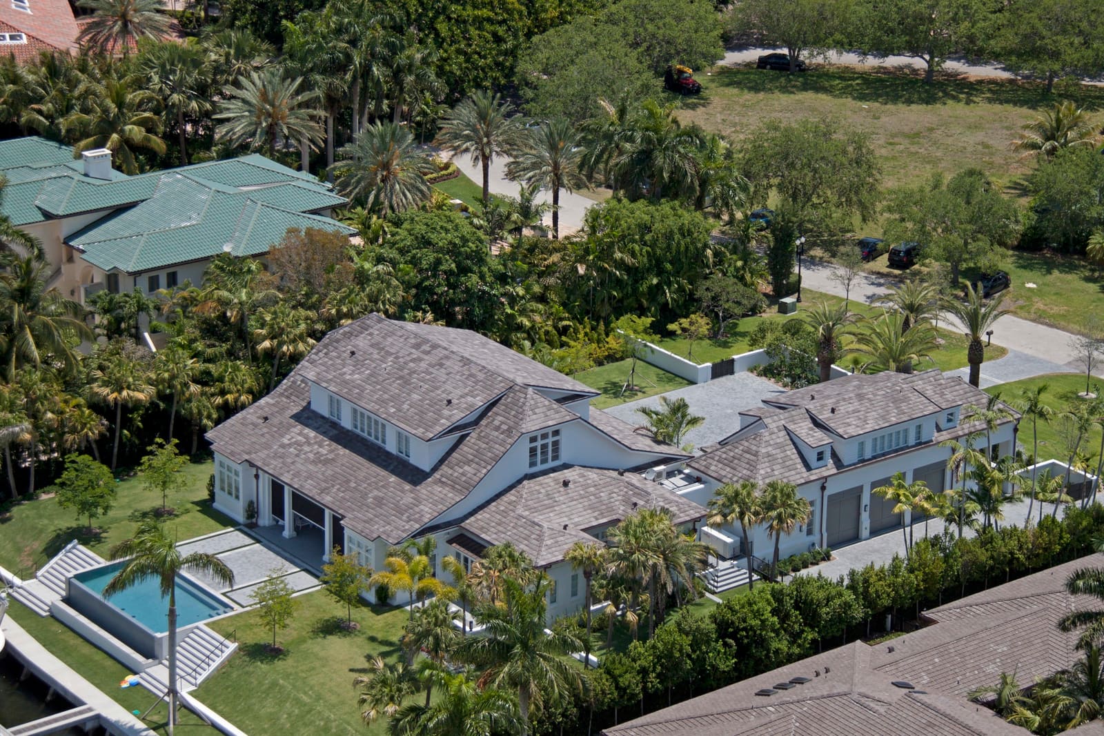 Aerial view of two luxury Miami homes with architectural asphalt shingle roofs, framed by palms and tropical landscaping.
