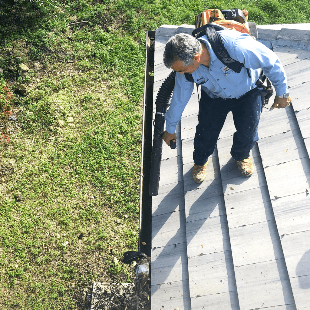 Roofer cleaning up the gutters with a leaf blower